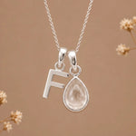 sterling silver initial f april birthstone natural clear quartz pendant necklace against a dark warm beige background