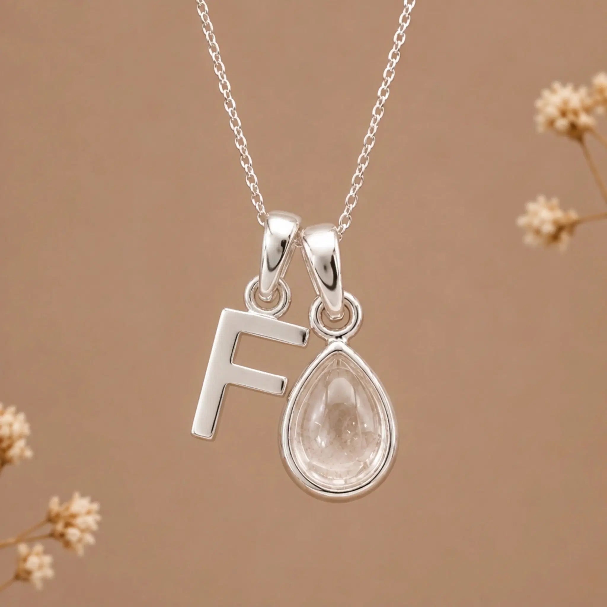 sterling silver initial f april birthstone natural clear quartz pendant necklace against a dark warm beige background