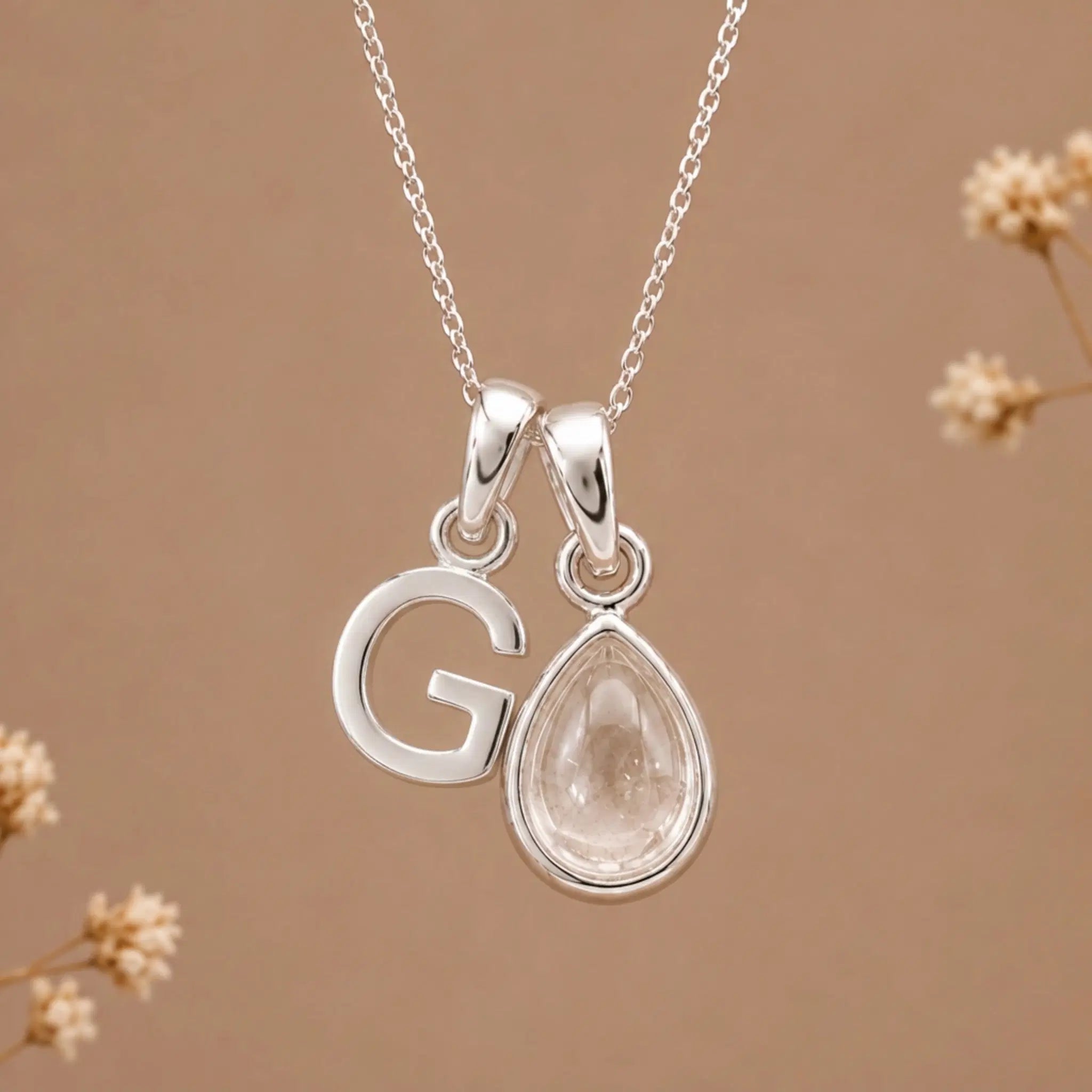 sterling silver initial g april birthstone natural clear quartz pendant necklace against a dark warm beige background