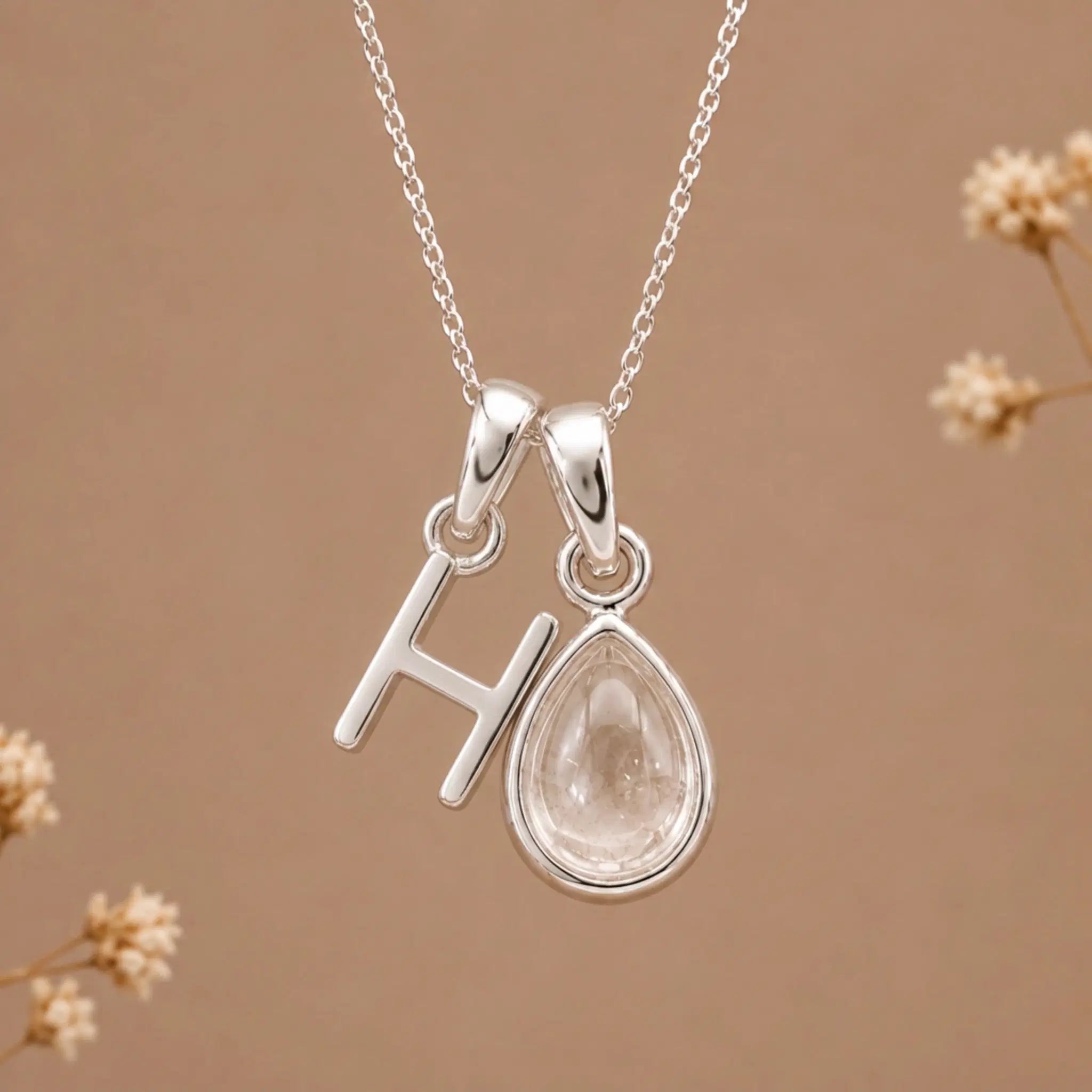 sterling silver initial h april birthstone natural clear quartz pendant necklace against a dark warm beige background
