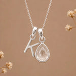 sterling silver initial k april birthstone natural clear quartz pendant necklace against a dark warm beige background