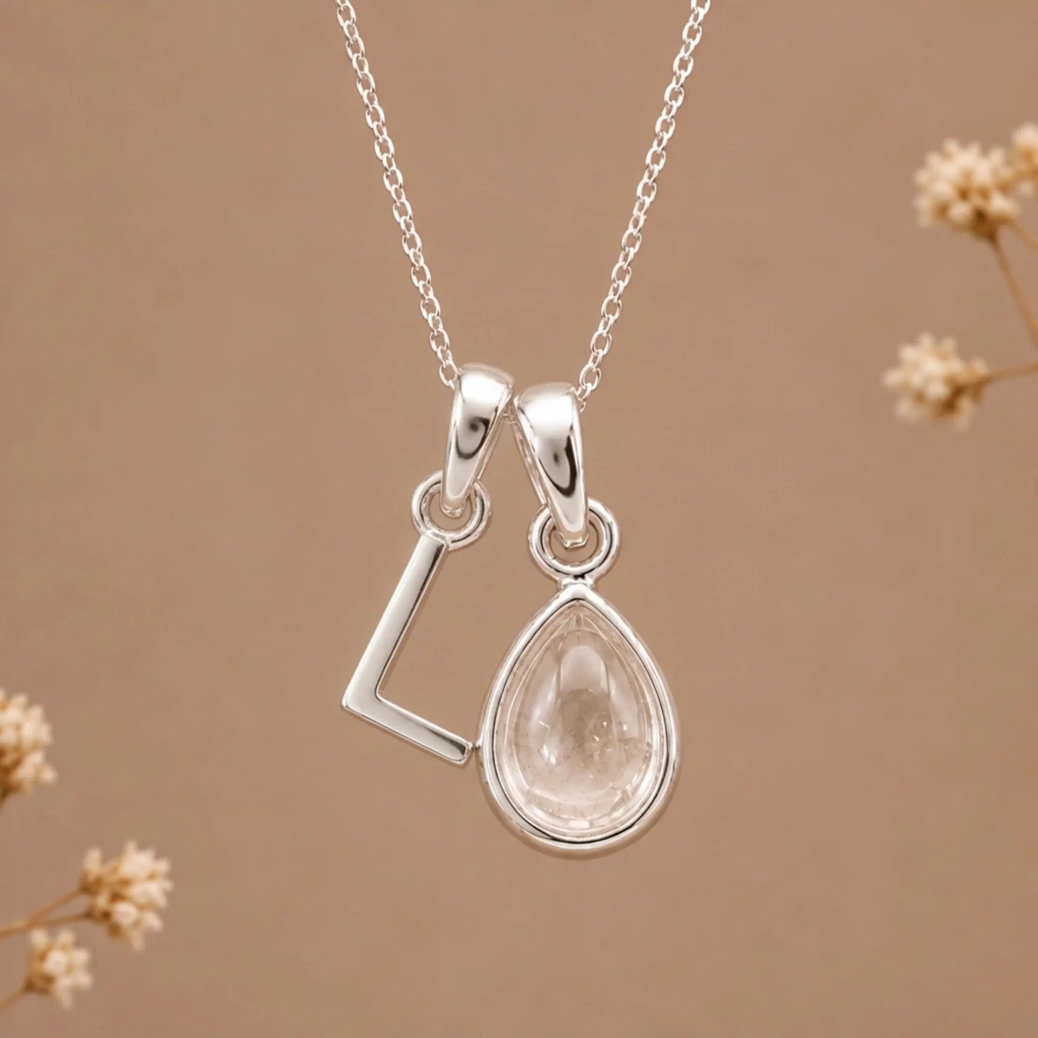 sterling silver initial l april birthstone natural clear quartz pendant necklace against a dark warm beige background