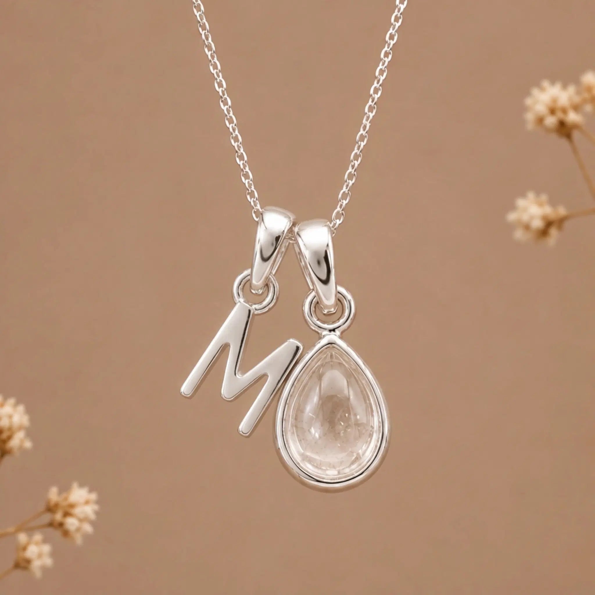 sterling silver initial m april birthstone natural clear quartz pendant necklace against a dark warm beige background