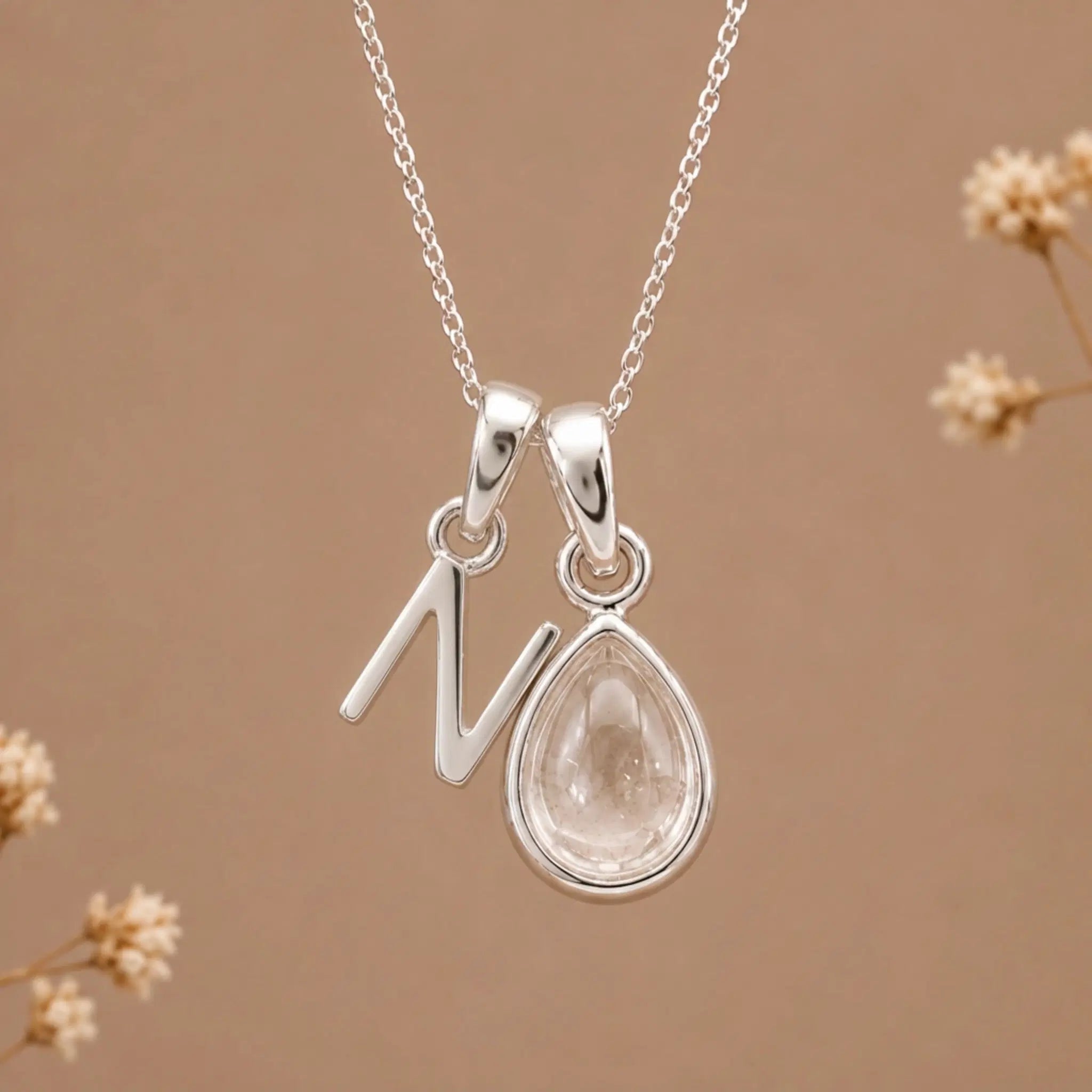 sterling silver initial n april birthstone natural clear quartz pendant necklace against a dark warm beige background