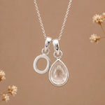 sterling silver initial o april birthstone natural clear quartz pendant necklace against a dark warm beige background
