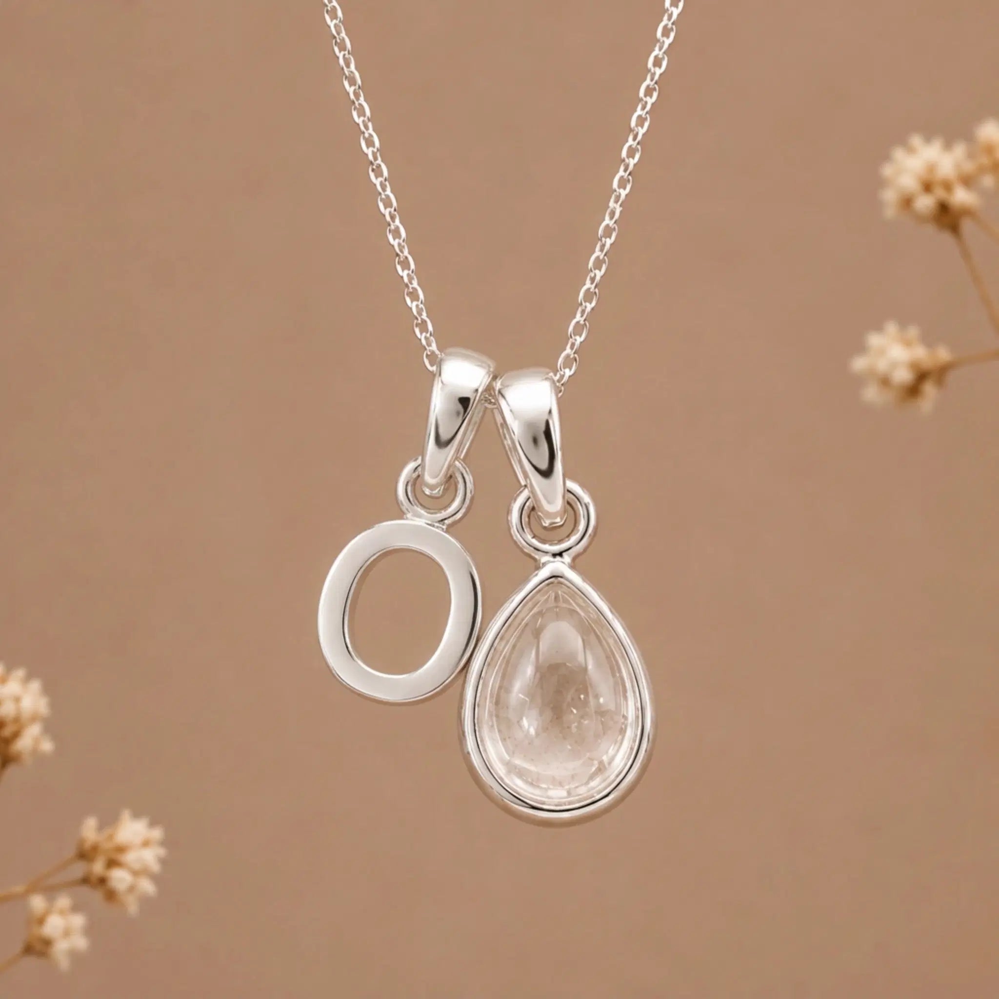 sterling silver initial o april birthstone natural clear quartz pendant necklace against a dark warm beige background