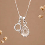 sterling silver initial d april birthstone natural clear quartz pendant necklace against a dark warm beige background