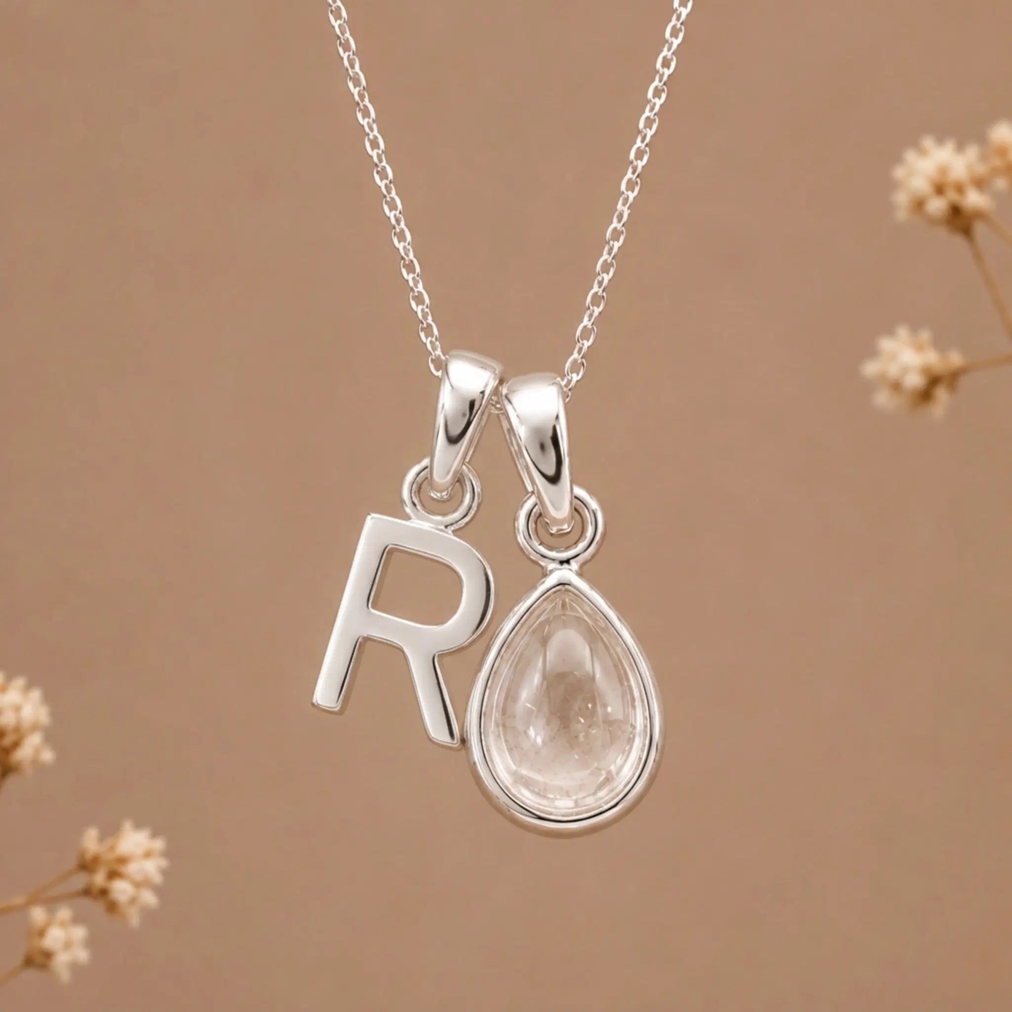 sterling silver initial r april birthstone natural clear quartz pendant necklace against a dark warm beige background