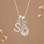 sterling silver initial s april birthstone natural clear quartz pendant necklace against a dark warm beige background
