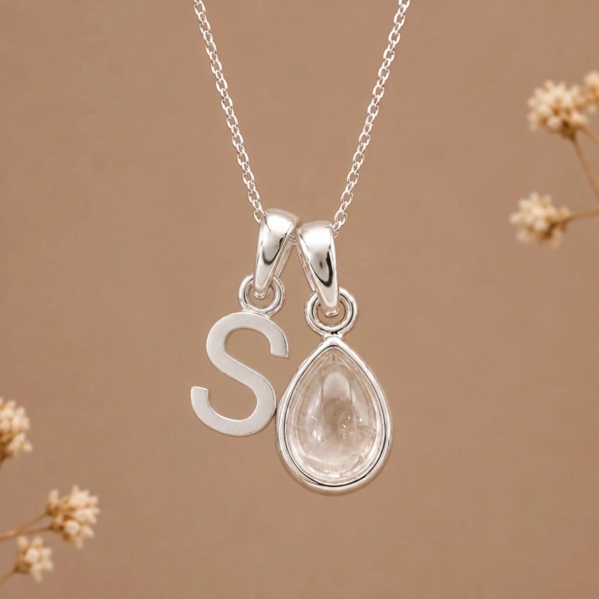 sterling silver initial s april birthstone natural clear quartz pendant necklace against a dark warm beige background