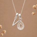 sterling silver initial v april birthstone natural clear quartz pendant necklace against a dark warm beige background