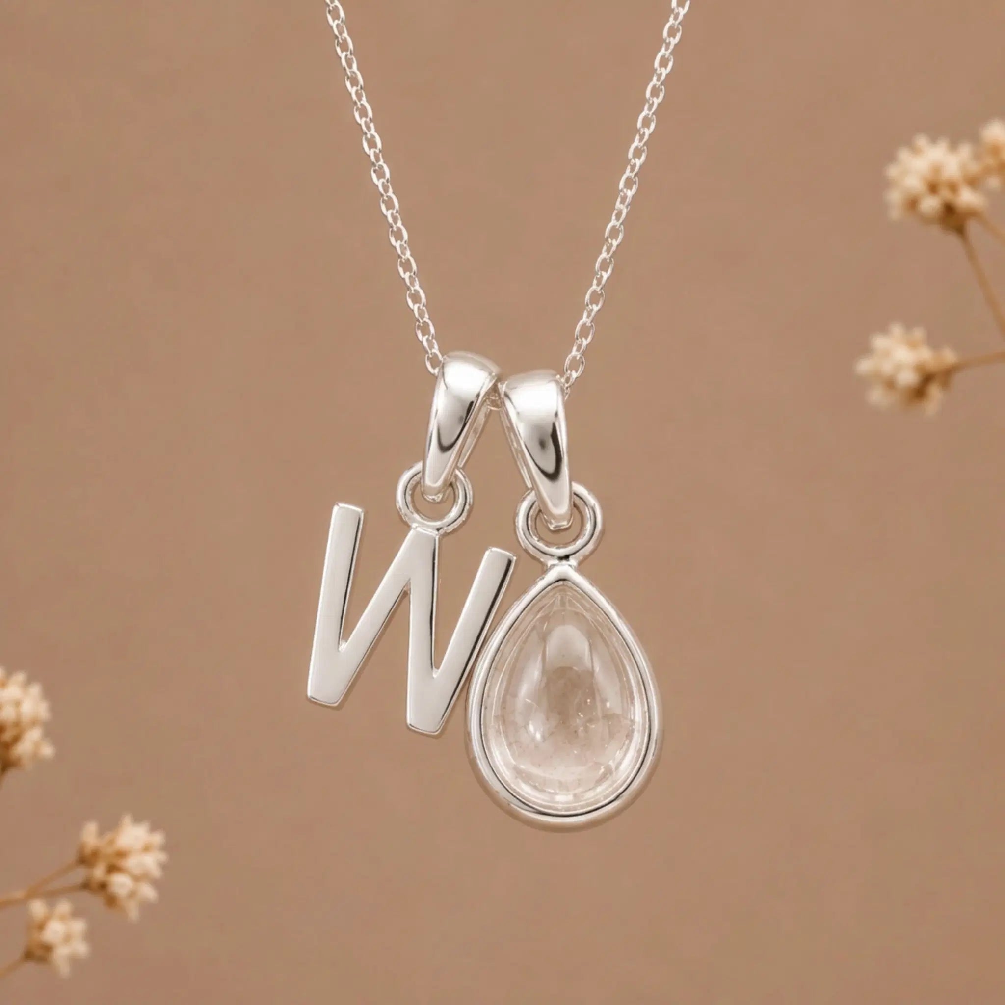 sterling silver initial w april birthstone natural clear quartz pendant necklace against a dark warm beige background