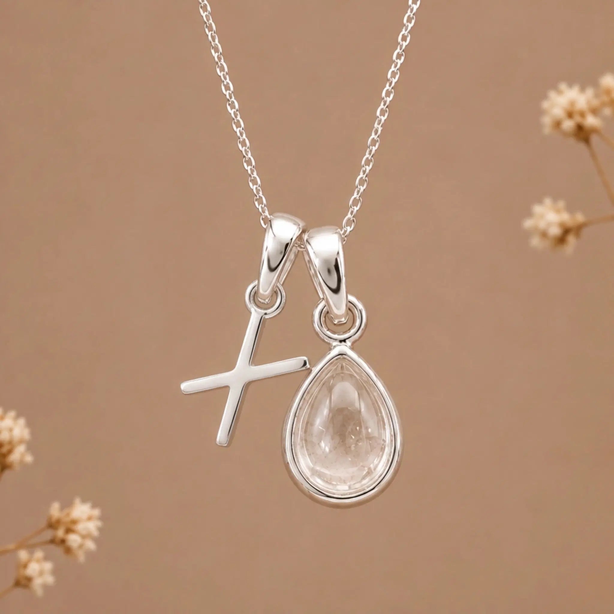 sterling silver initial x april birthstone natural clear quartz pendant necklace against a dark warm beige background