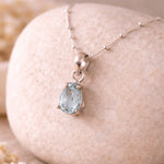 Silver aquamarine necklace with a teardrop-shaped blue aquamarine gemstone pendant on a stone surface.