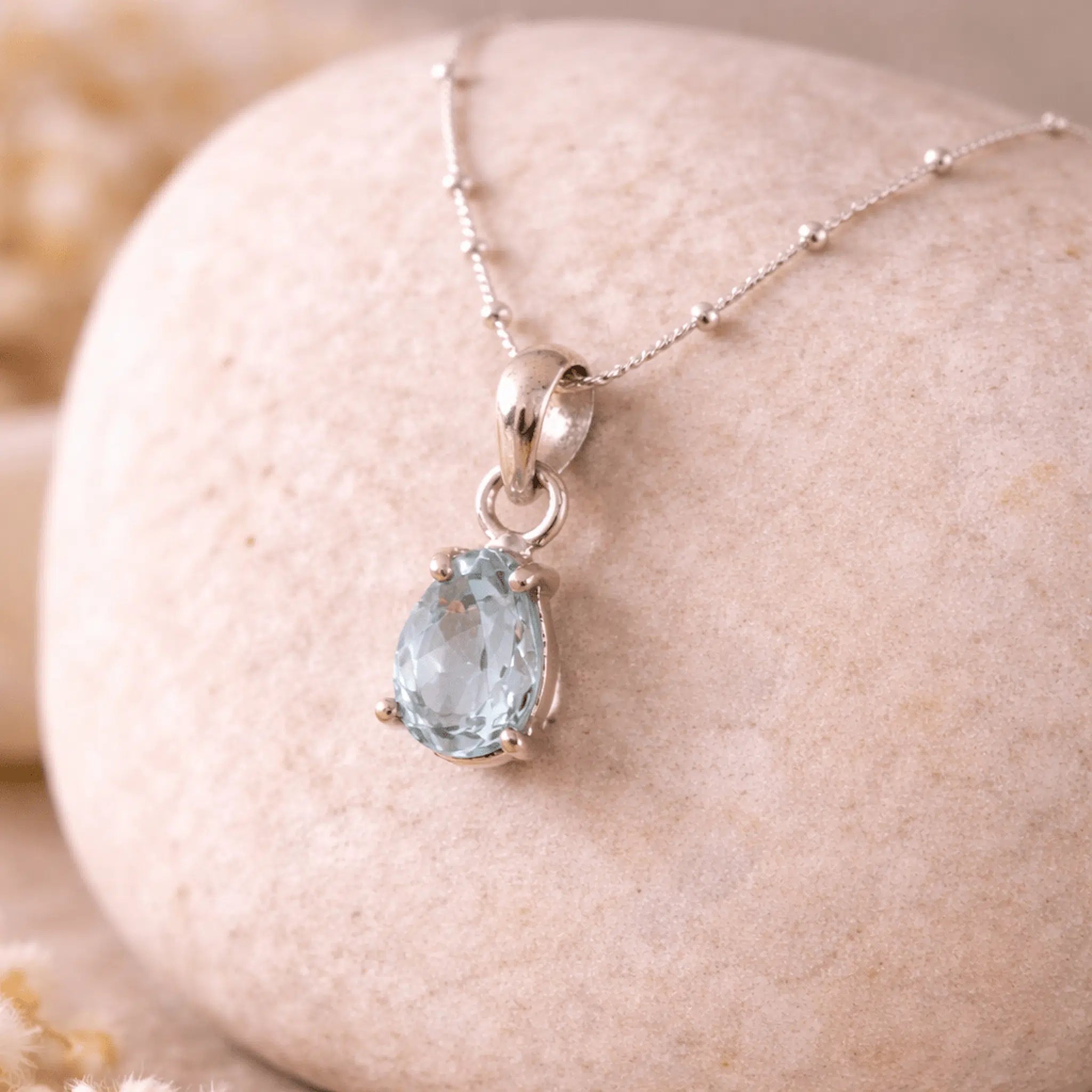 Silver aquamarine necklace with a teardrop-shaped blue aquamarine gemstone pendant on a stone surface.