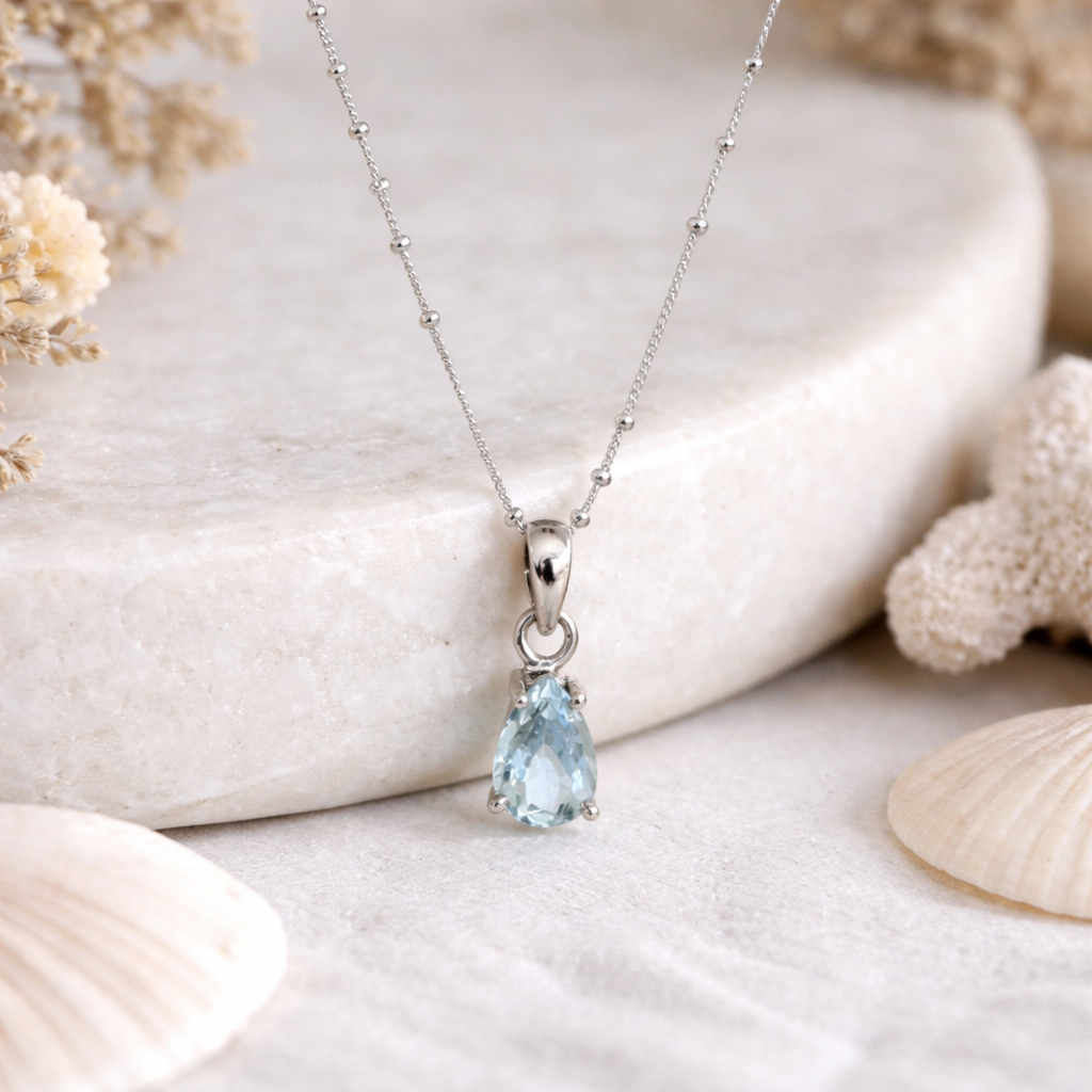 Silver necklace with a teardrop-shaped blue aquamarine gemstone pendant on a natural stone background.
