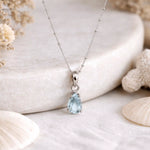 Silver aquamarine necklace with a teardrop-shaped blue aquamarine gemstone pendant on a natural stone background.