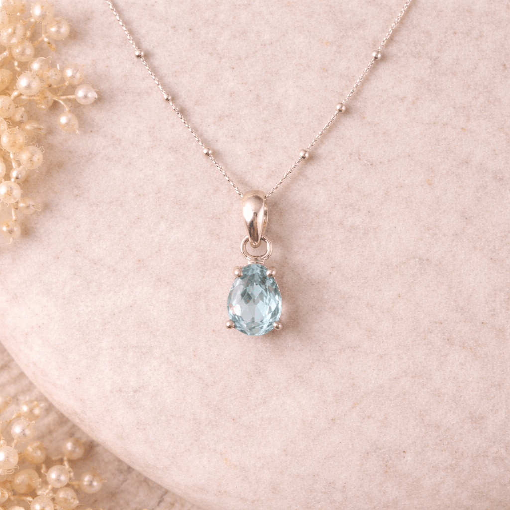 Necklace with a teardrop-shaped blue gemstone pendant on a soft pink background