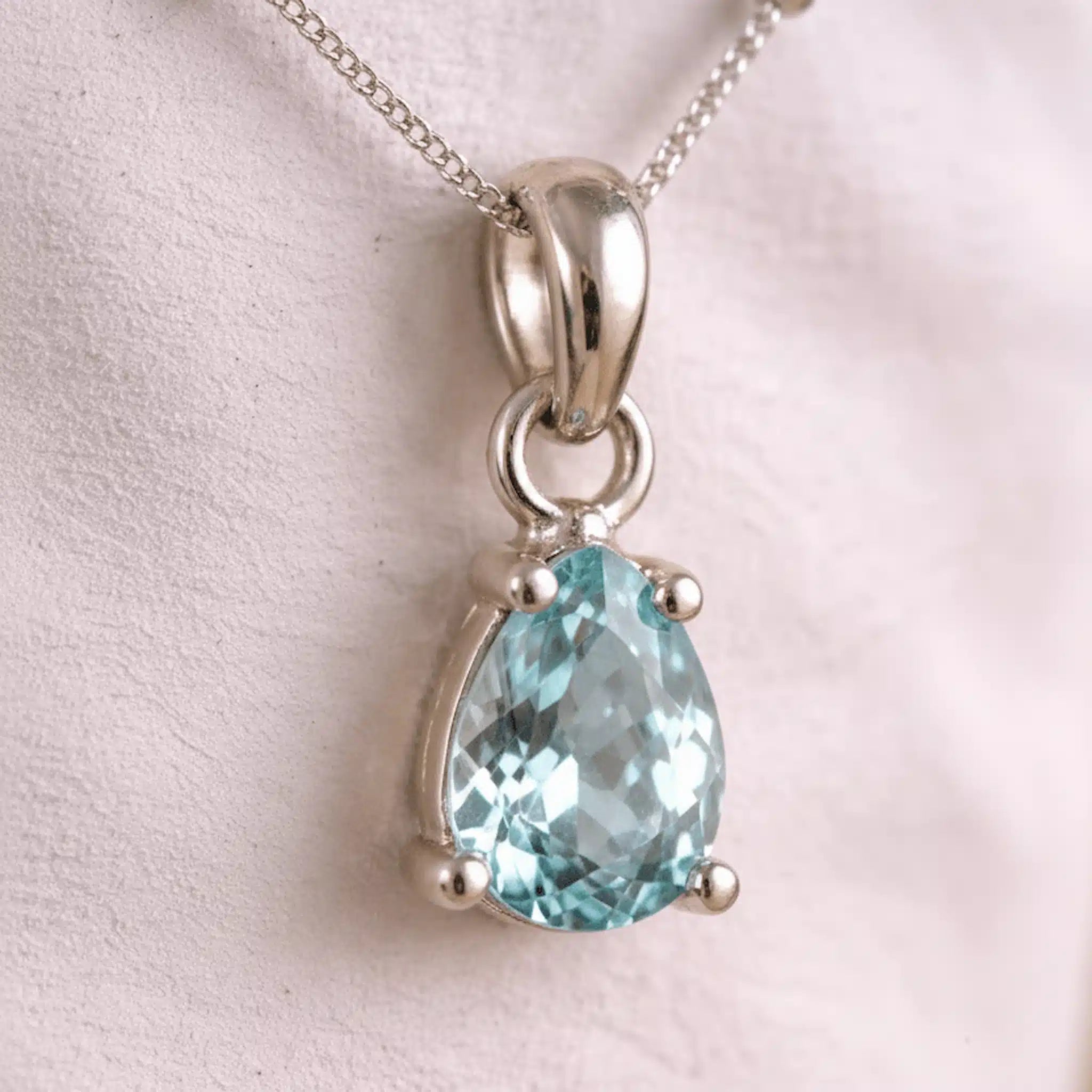 Silver aquamarine necklace with a teardrop-shaped blue aquamarine gemstone on a light pink background