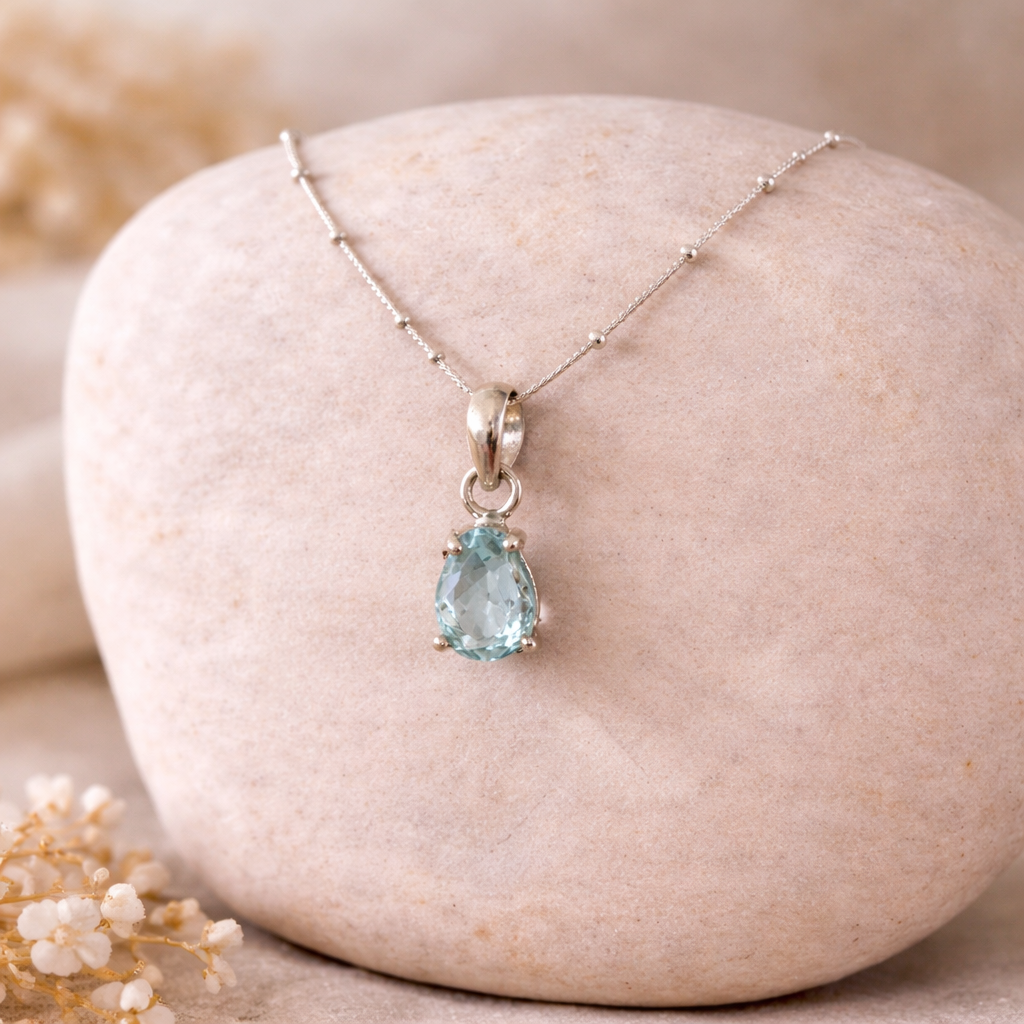 Teardrop-shaped faceted aquamarine gemstone necklace on a stone surface with blurred background