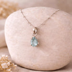 Teardrop-shaped faceted aquamarine necklace on a stone surface with blurred background