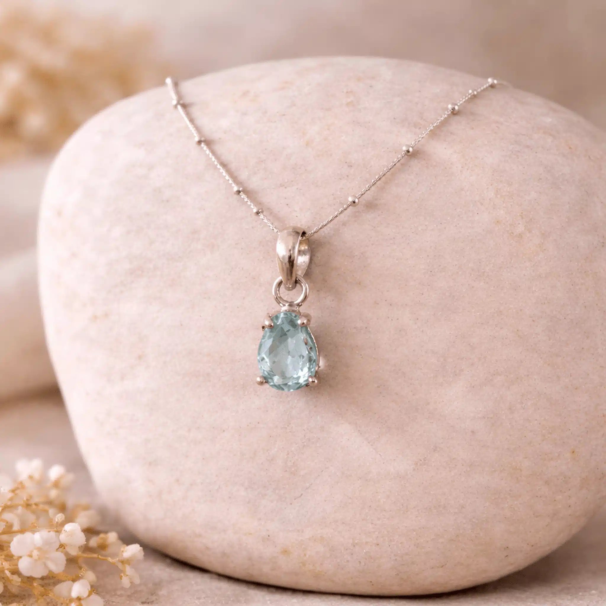 Teardrop-shaped faceted aquamarine necklace on a stone surface with blurred background