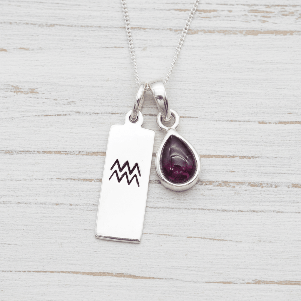 Silver necklace with Aquarius zodiac pendant and tear drop natural garnet gemstone pendant on a light wooden surface
