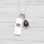 Silver necklace with Aquarius zodiac pendant and tear drop natural garnet gemstone pendant on a light wooden surface