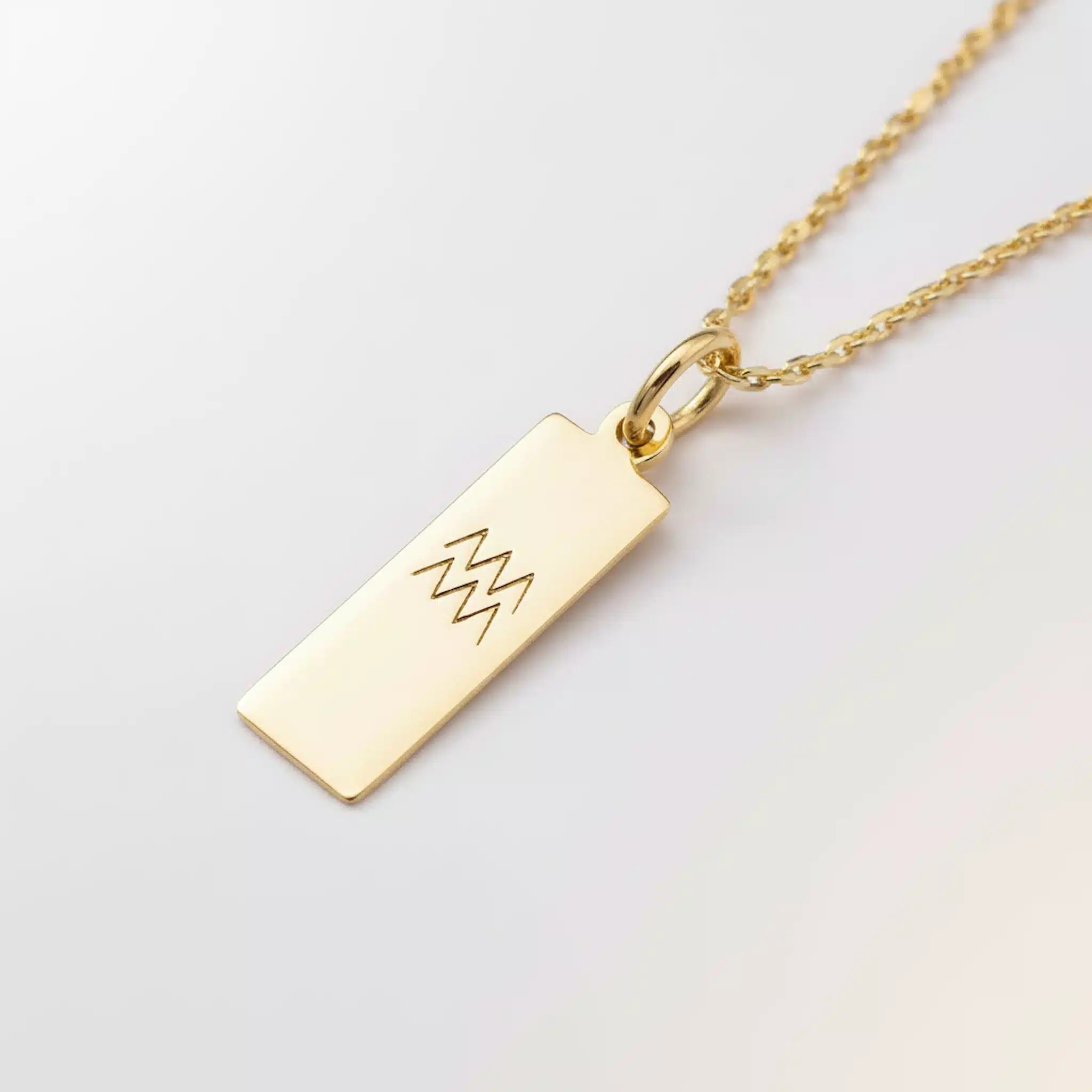 Gold necklace with a rectangular pendant on a light gray background