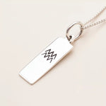 Silver necklace with a rectangular pendant featuring a black design on a beige background