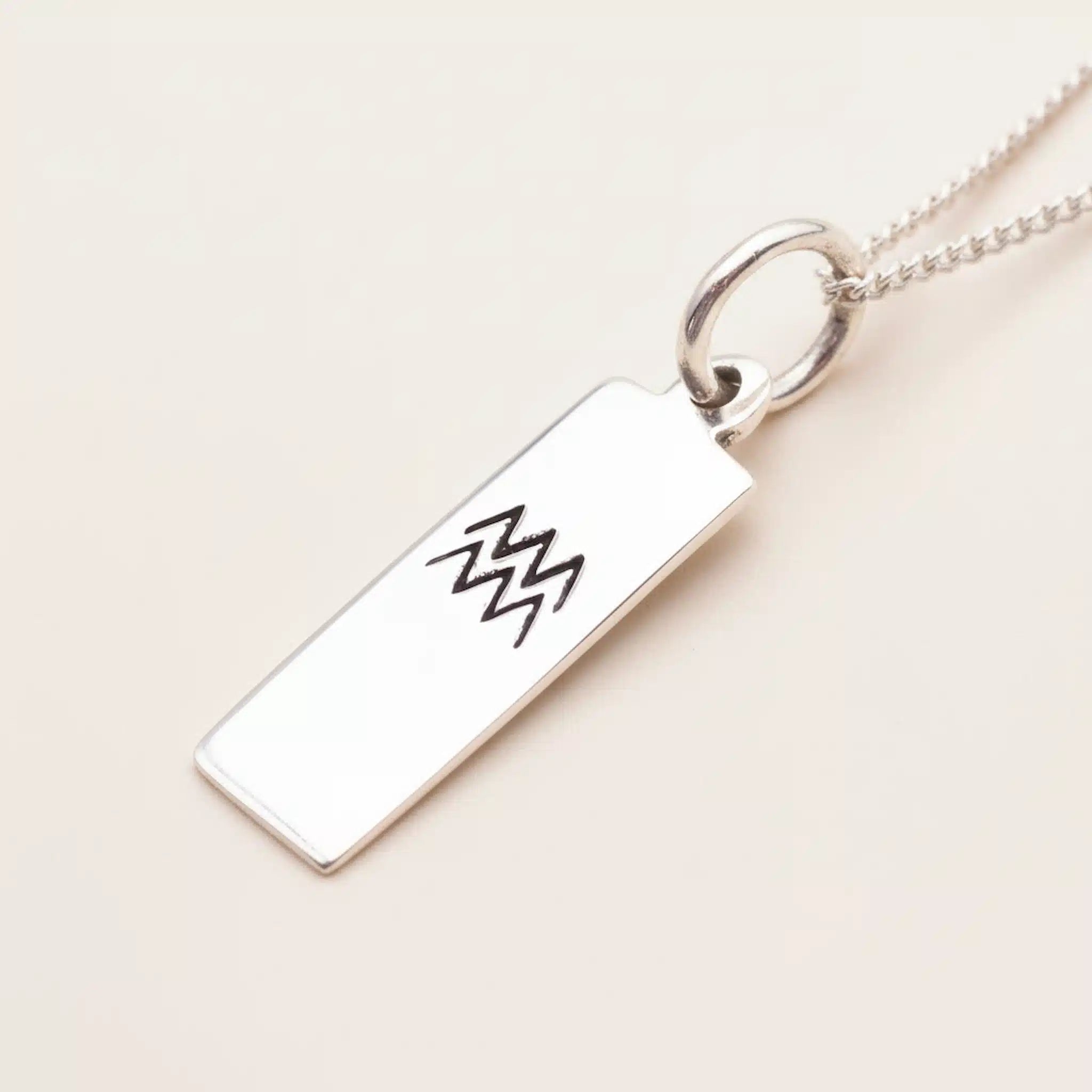 Silver necklace with a rectangular pendant featuring a black design on a beige background