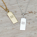 Gold and silver pendant necklaces with Aquarius zodiac symbols on a textured surface.