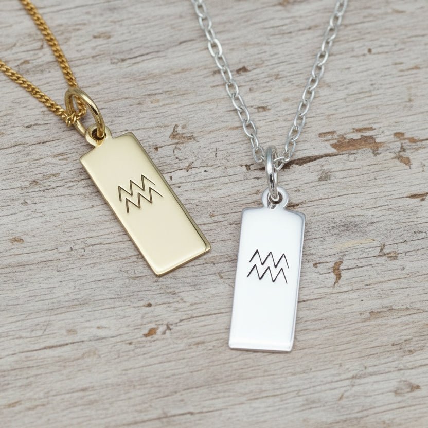 Gold and silver pendant necklaces with Aquarius zodiac symbols on a textured surface.