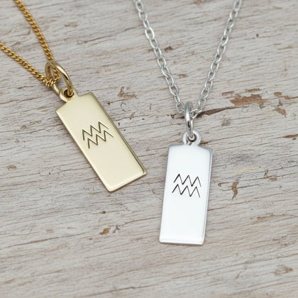 Gold and silver pendant necklaces with Aquarius zodiac symbols on a textured surface.
