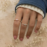 Hand wearing two gold rings with small stones against a natural background