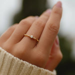 Close-up of a hand wearing a gold ring with cubic zirconias on a blurred background