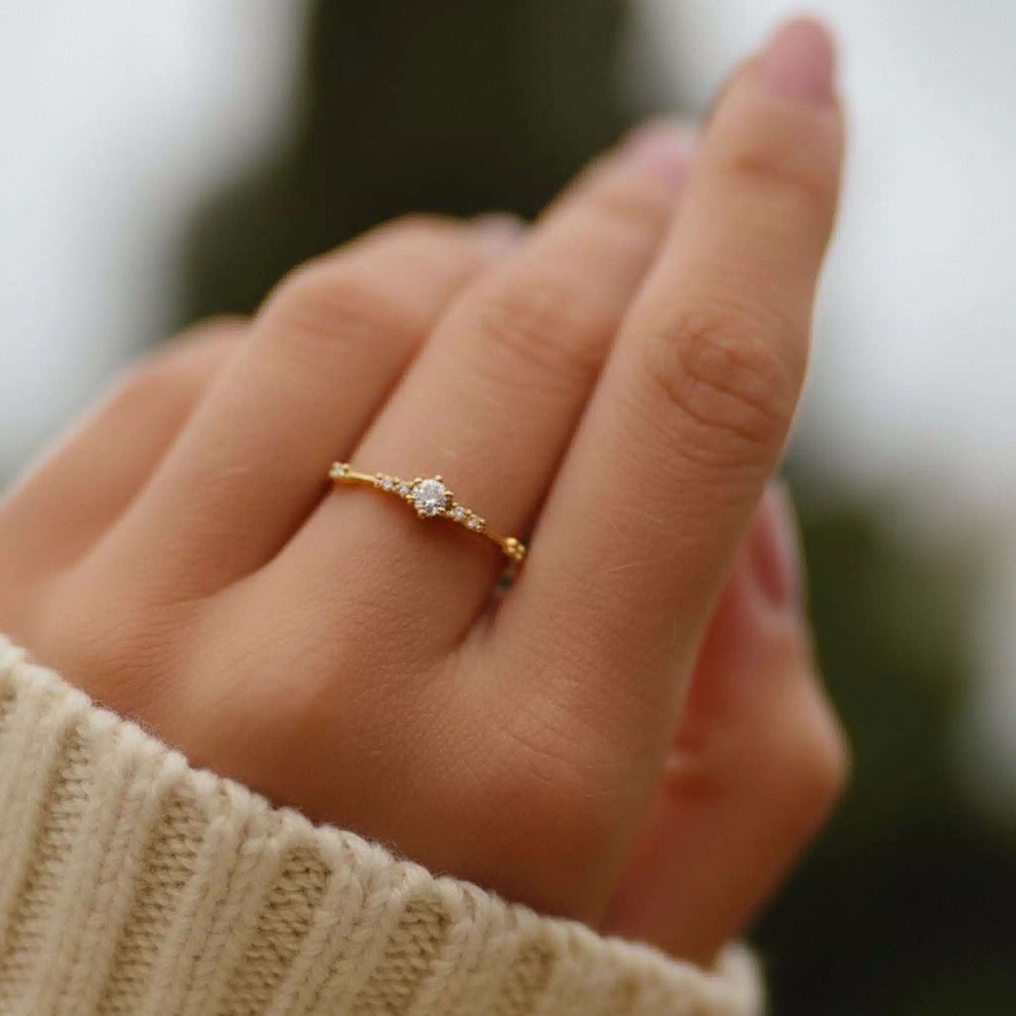 Close-up of a hand wearing a gold ring with cubic zirconias on a blurred background