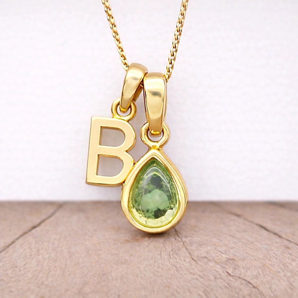 Close-up of personalised gold-plated B initial charm and light green pear-shaped peridot pendant on a fine chain, August birthstone necklace