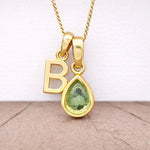 Close-up of personalised gold-plated B initial charm and light green pear-shaped peridot pendant on a fine chain, August birthstone necklace
