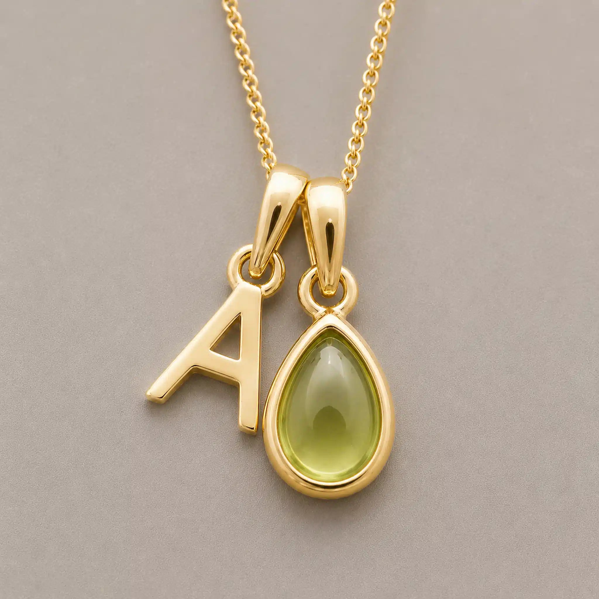 Close-up of personalised gold-plated A initial charm and light green pear-shaped peridot pendant on a fine chain, August birthstone necklace