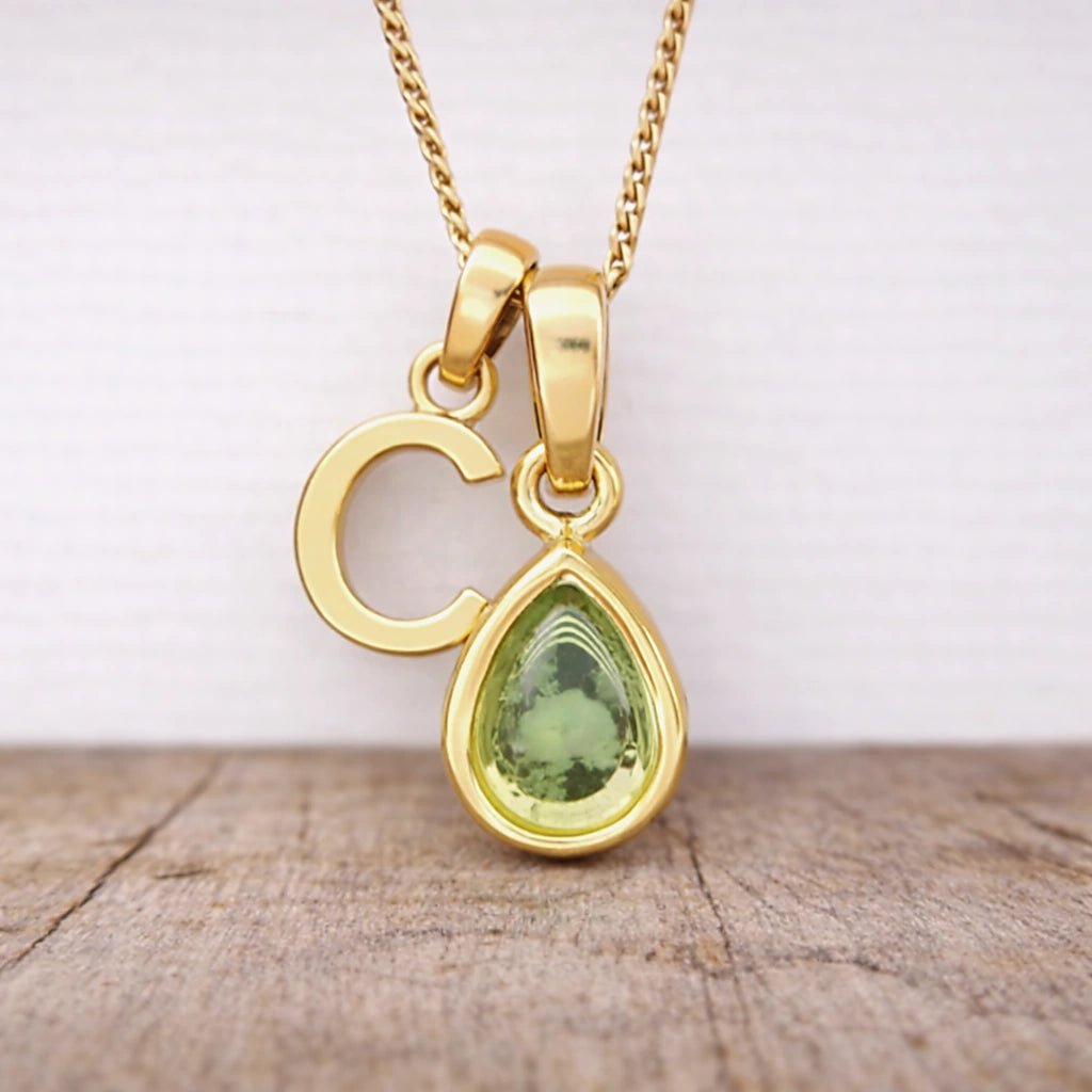Close-up of personalised gold-plated C initial charm and light green pear-shaped peridot pendant on a fine chain, August birthstone necklace