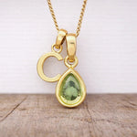 Close-up of personalised gold-plated C initial charm and light green pear-shaped peridot pendant on a fine chain, August birthstone necklace