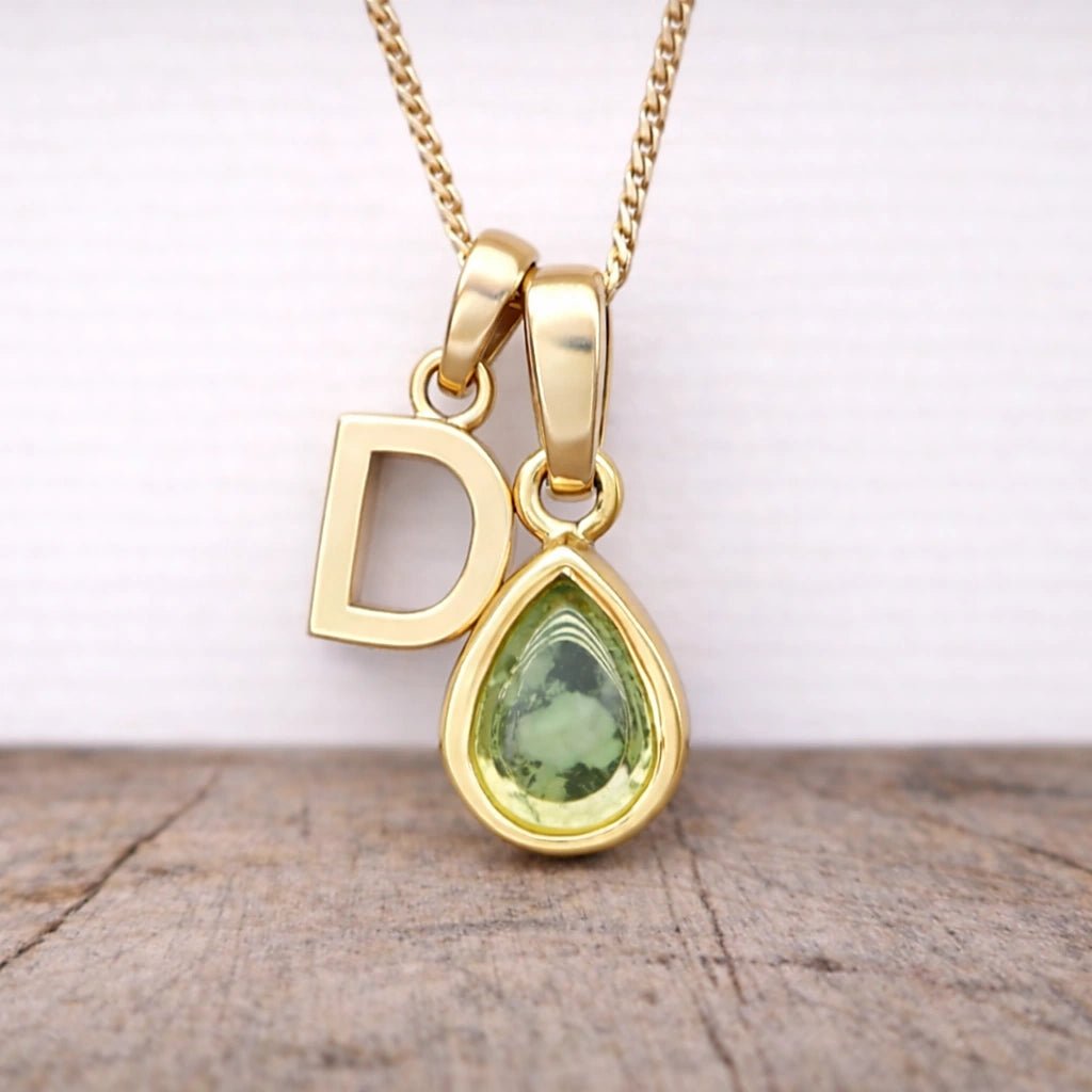 Close-up of personalised gold-plated D initial charm and light green pear-shaped peridot pendant on a fine chain, August birthstone necklace