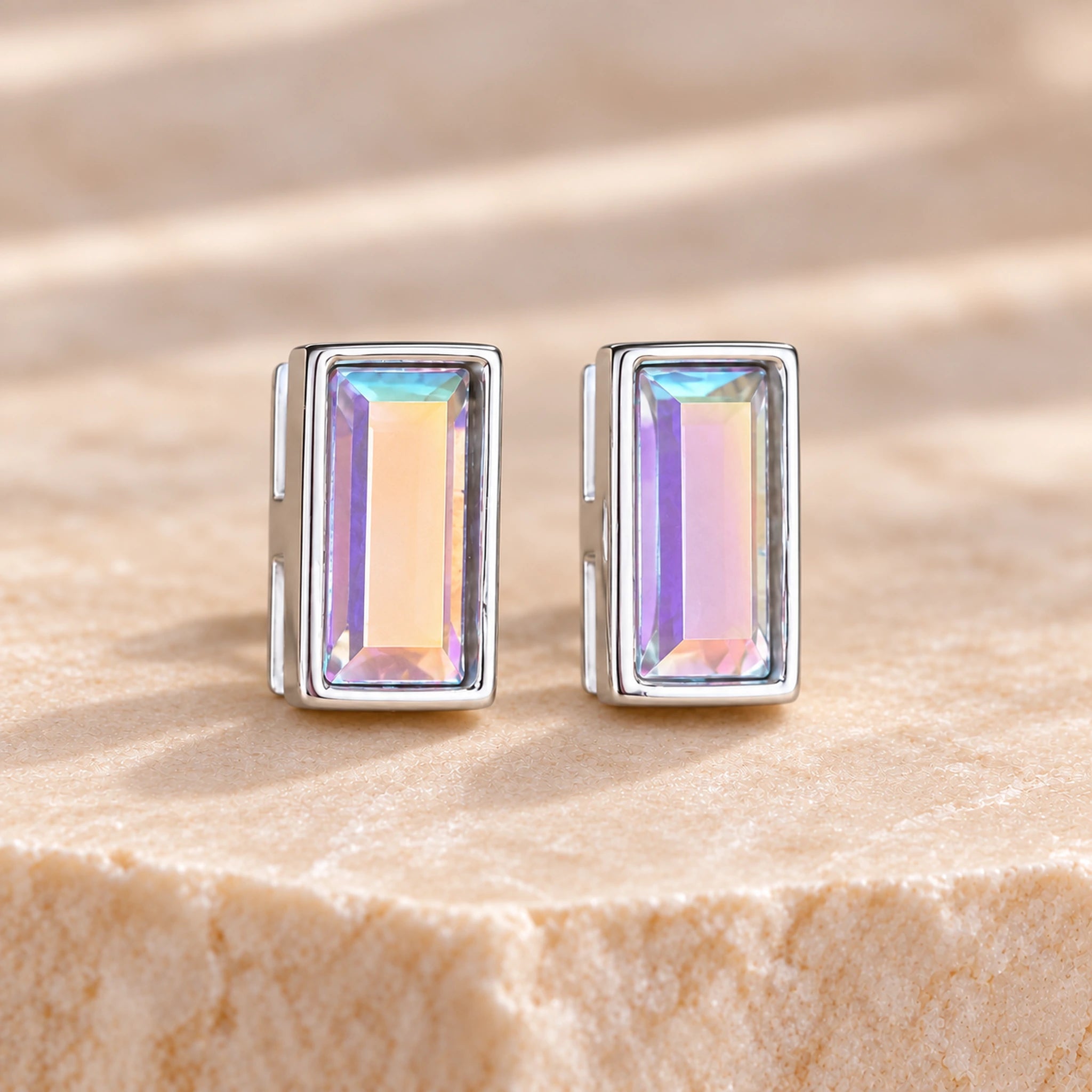 Pair of Aurore Boreale iridescent Austrian crystal baguette stud earrings in rhodium-plated 925 sterling silver, showing champagne, pink and rainbow flashes in slim rectangular bezels