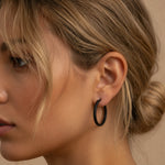 Close-up of a person wearing a large black hoop earring with a neutral background
