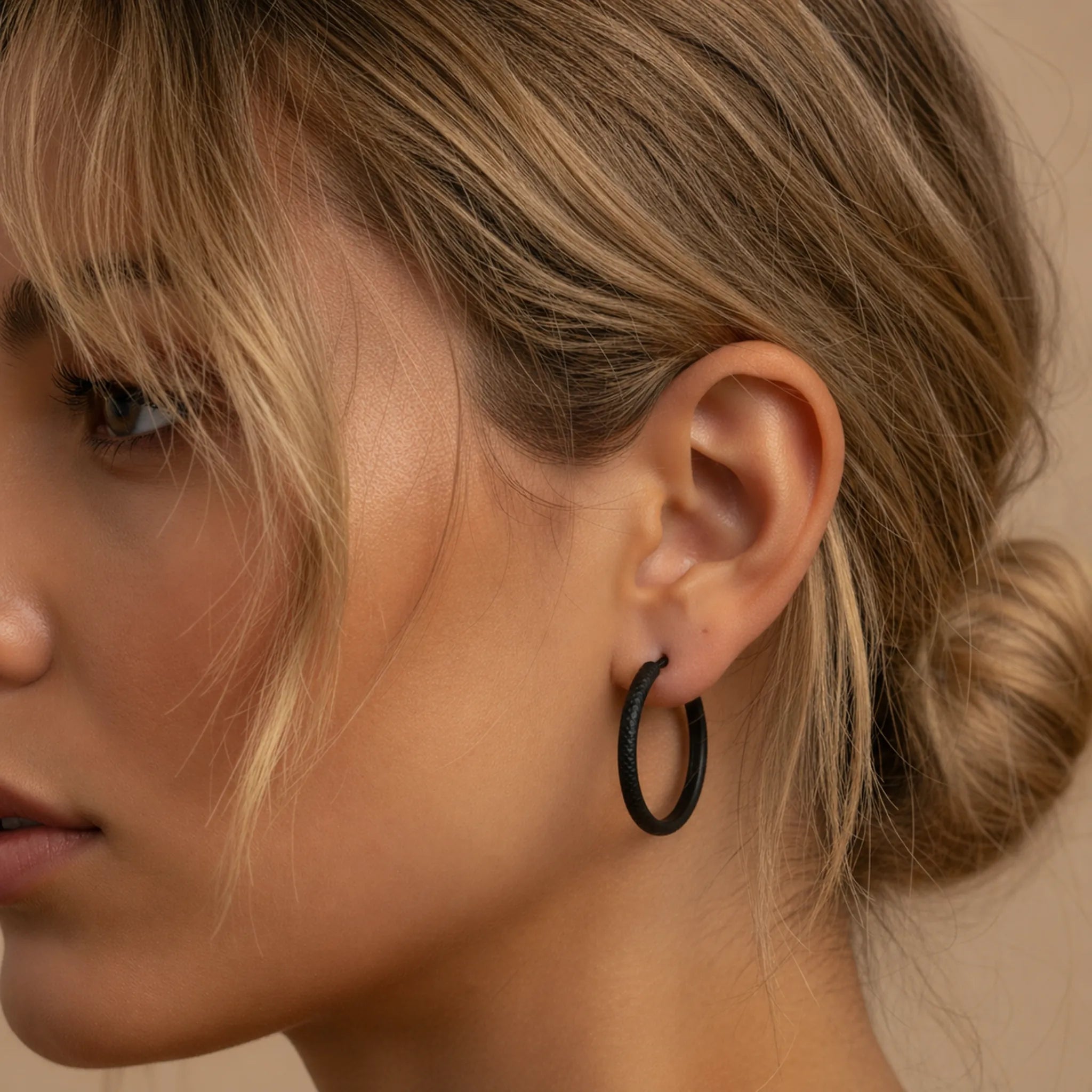 Close-up of a person wearing a large black hoop earring with a neutral background