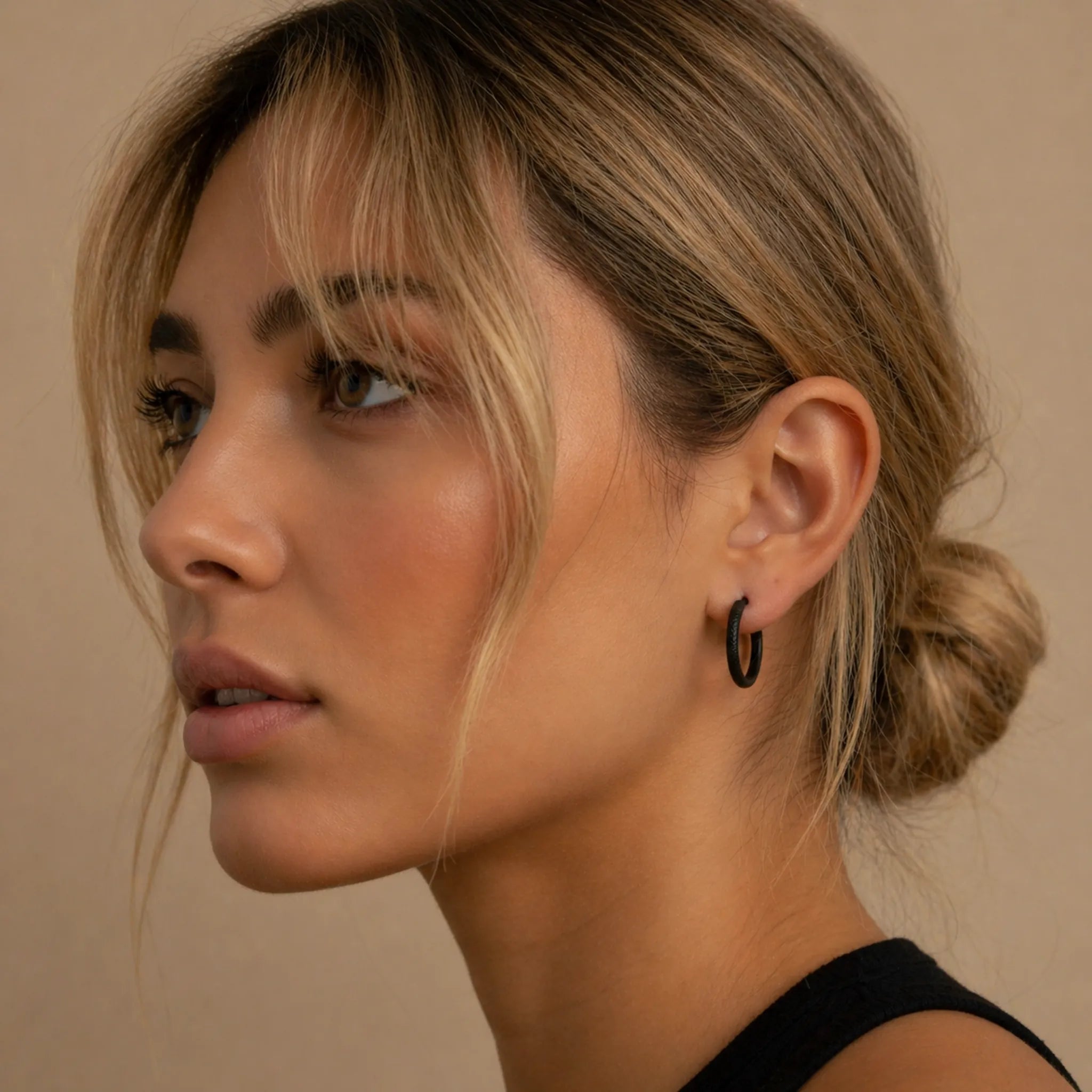 Close-up of a woman with styled hair and waterproof black hoop earrings against a neutral background