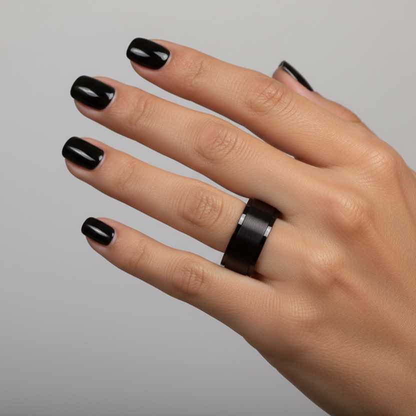 Hand with black nail polish wearing a black ring on a gray background