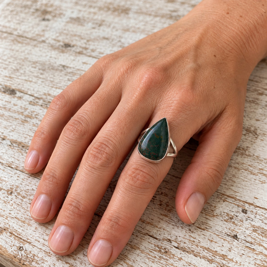 Hand wearing the silver bloodstone teardrop ring on whitewashed wood