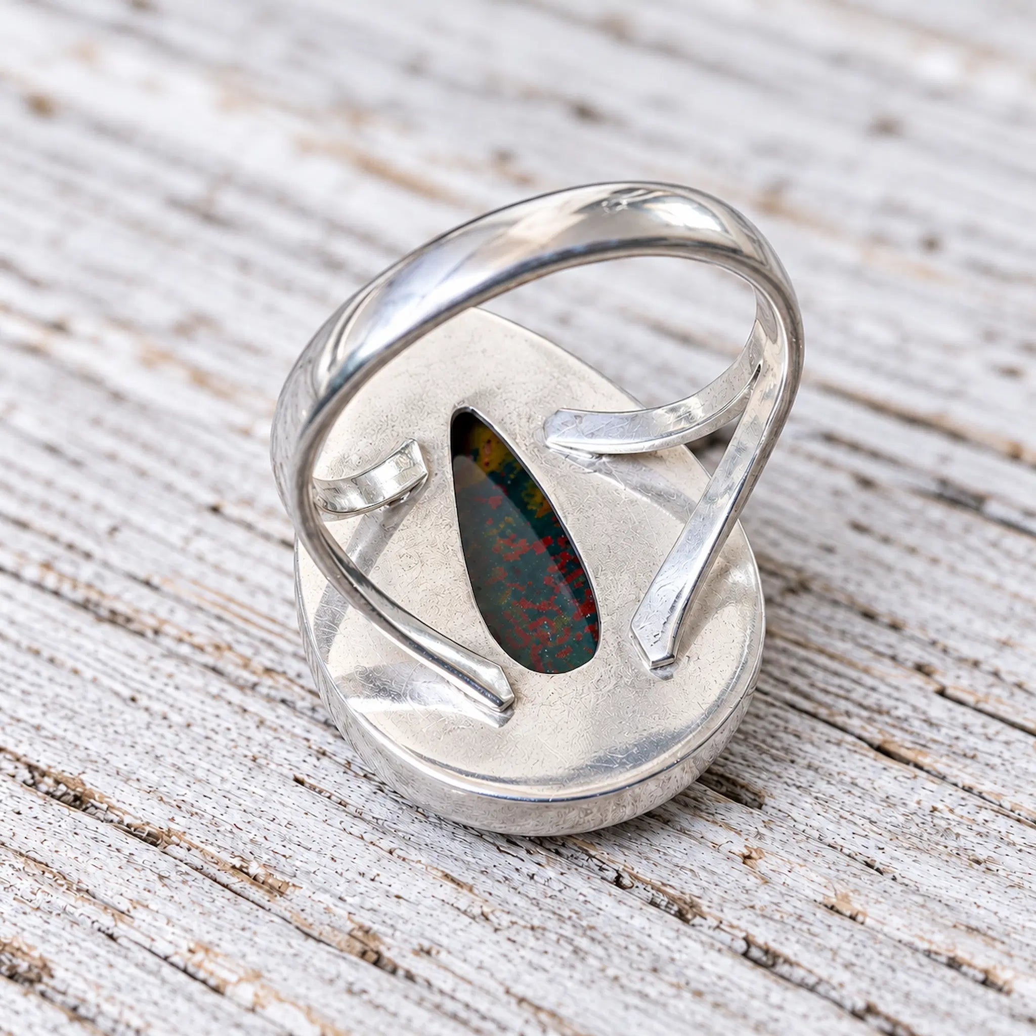 Back view of the bloodstone teardrop ring showing the open silver setting on whitewashed wood